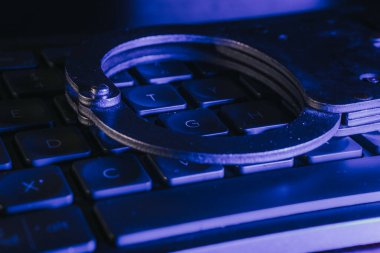 Mavi ışıkla vurgulanan bir klavyeye konulan kelepçeler, suç, adalet ve teknoloji ile kolluk kuvvetlerinin kesişme noktalarını temsil ediyor.