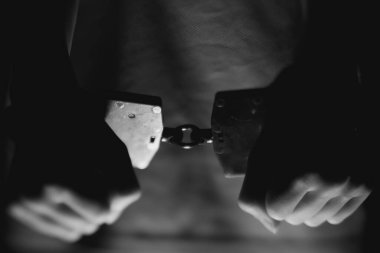 Bireyin elleri kelepçelidir, düşük aydınlık bir ortamda yakalanır, durumun katıksız kontrastını ve duygusal yoğunluğunu vurgular.