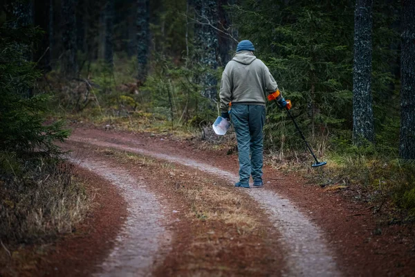 Metal dedektörlü bir adam ağaçlar ve çalılıklarla çevrili bir ormanda dolambaçlı bir yolda yürüyor. Doğada saklı hazineleri arıyor.