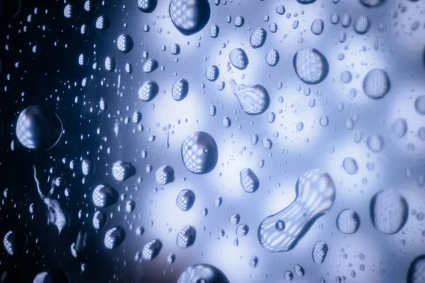 Camdaki su damlacıkları, ışığı yansıtan ve eşsiz şekiller oluşturan, doğal elementlerin ve dokuların güzelliğini vurgulayan soyut bir desen oluştururlar.