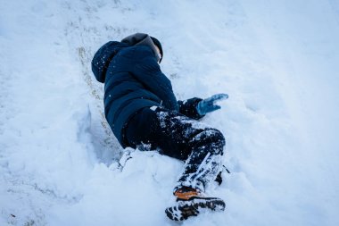 Kışın giydiği çocuk kardan zevk alıyor, bir tepeden kayıyor, kış manzarası ile çevrili, eğlenceli açık hava aktivitelerinin özünü yakalıyor.