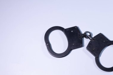 Temiz beyaz bir zeminde sergilenen kelepçeler, metalik bitiş ve tasarımlarını vurguluyor, kolluk kuvvetleri ve güvenlik temalarını basit bir kompozisyonda temsil ediyor