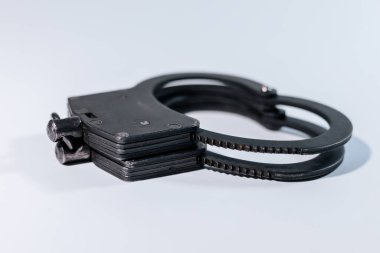 Hafif bir zeminde sergilenen kelepçeler, metalik bitiş ve tasarımlarını vurguluyor, yasa uygulama, güvenlik ve adalet temaları temsil ediyor