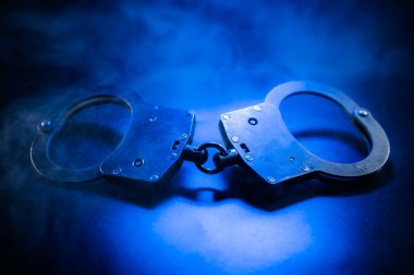 Kelepçeler, mavi ışıkla vurgulanmış karanlık bir yüzeye yerleştirilmiş, büyüleyici bir sahnede kolluk kuvvetleri, adalet ve otorite temaları çağrıştırıyor.