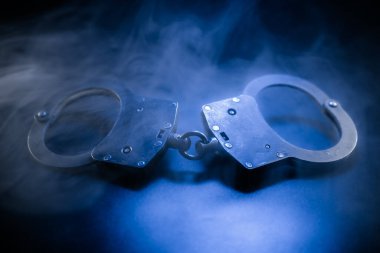 Karanlık yüzeye yerleştirilmiş kelepçeler, dumanla kaplanmış ve mavi ışıkla aydınlatılmış, karamsar ve yoğun bir sahne yaratarak hapsetme ve gerilim hissi uyandırıyor.