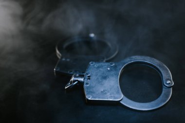 Karanlık bir zemine yerleştirilmiş kelepçeler, hafif bir sis, kanun uygulama, adalet temaları ve suçun ve cezanın karmaşık doğasını temsil ediyor.