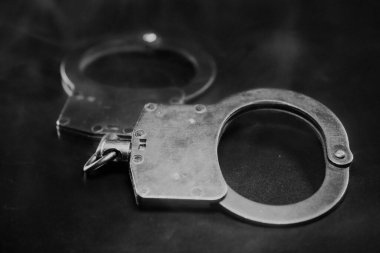 Metalik kelepçeler karanlık bir yüzeye yerleştirilerek yansıtıcı yüzeyleri ve karmaşık tasarımı vurgulanıyor, kanun uygulama ve adalet temaları çağrıştırıyor