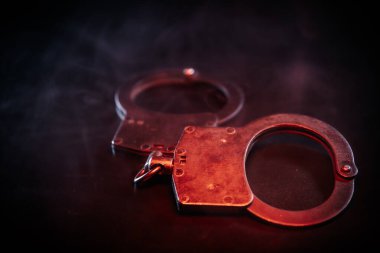 Metalik kelepçeler, kırmızı ışıkla vurgulanmış, kolluk kuvvetleri ve otorite temalarını yansıtan çarpıcı bir ortam yaratıyor.