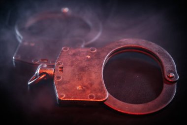 Karanlık bir yüzeye yerleştirilmiş kelepçeler, dramatik aydınlatma ve dumanla güçlendirilmiş, büyüleyici bir sahnede kolluk kuvvetleri, adalet ve otorite temaları çağrıştırıyor