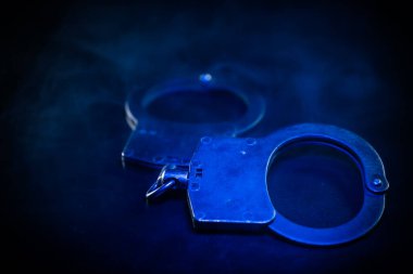 Metalik kelepçeler koyu bir yüzeyde, mavi ışıkla aydınlatılmış, karmaşık tasarımı vurguluyor ve güvenlik ve kolluk kuvvetlerinin atmosferini yansıtıyor.