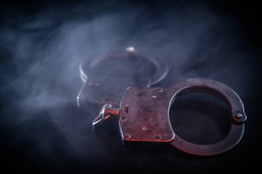 Karanlık bir arka plana yerleştirilmiş kelepçeler, dumanla kaplanmış, metalik dokularını vurguluyor ve suç ve kolluk kuvvetleriyle ilgili dengesiz bir ortam yaratıyor.