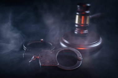 Gavel, karanlık yüzeyde kelepçelerin yanına yerleştirildi. Ortalıkta duman uçuşuyordu. Adaleti ve hukuk sistemini temsil eden dramatik bir sahne yaratıyordu.