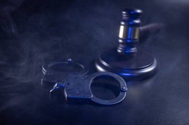 Gavel ve kelepçeler karanlık bir yüzeye yerleştirildi. Kanun uygulama, adalet ve hukuk sisteminin dramatik bir atmosferdeki temalarını gözler önüne serdi.