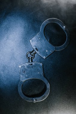 Karanlık bir yüzeye yerleştirilmiş kelepçeler, metalik bitiş ve karmaşık tasarımı vurguluyor, yasa uygulama ve güvenlik tedbirleri temalarını temsil ediyor