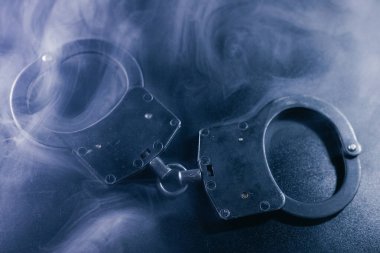 Karanlık bir yüzeye girdap dumanı ile yerleştirilen kelepçeler, suç, adalet ve kolluk kuvvetleri temalarını çağrıştıran dramatik bir sahne yaratıyor.