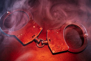 Koyu renkli bir yüzeye yerleştirilmiş kelepçeler, dönen dumanla kaplanmış, otoritenin temaları ve kısıtlamalarını vurgulayan dengesiz bir ortam yaratıyor.