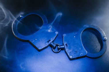 Karanlık bir yüzeye yerleştirilmiş kelepçeler etrafta uçuşan dumanlar adaletin temaları ve kısıtlamaları vurgulayan dengesiz bir ortam yaratıyor.