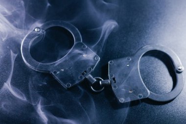 Karanlık bir yüzeye yerleştirilmiş kelepçeler, dumanla kaplanmış, kanun ve adalet temalarını vurgulayan gizemli bir ortam yaratıyor.