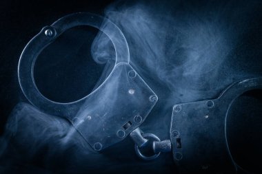 Karanlık yüzeye girdap dumanı ile kelepçelenmiş, gizemli bir ortam yaratıyor, çarpıcı bir kompozisyonda kolluk kuvvetleri, adalet ve otorite temalarını temsil ediyor