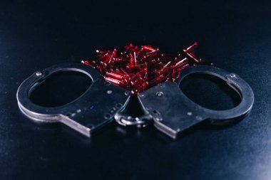 Koyu bir arka plana kelepçelenmiş, kırmızı boncuklarla çevrili, hapsedilme ve özgürlük temalarını temsil eden, görsel olarak ilgi çekici bir sahne yaratıyor.