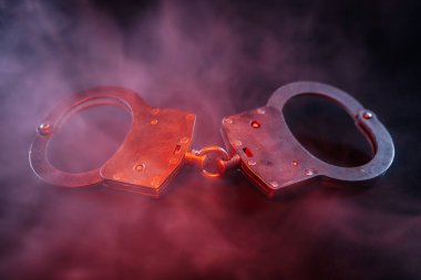 Karanlık bir yüzeyde dinlenen kelepçeler, renkli dumanla kaplanmış, hapsetme ve gerilim hissi uyandırıyor, sahnenin dramatik görsel etkisini arttırıyor.