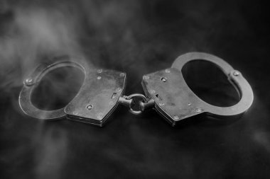 Karanlık bir arka plana yerleştirilmiş kelepçeler, dumanla kaplanmış, adalet ve otorite temaları çağrıştırıyor, kısıtlama ve kontrolün görsel anlatımını geliştiriyor.