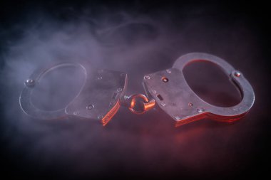 Kelepçeler, etrafta dönen dumanların dramatik etkisini artırdığı ve kanun uygulama ve adalet temalarını sembolize ettiği karanlık bir yüzeye yerleştiriliyor.