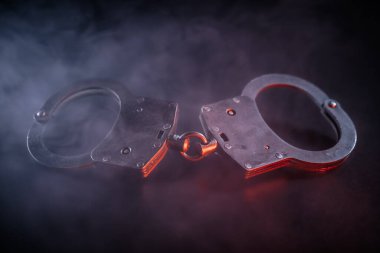 Kelepçeler, kolluk kuvvetleri, adalet ve kısıtlama temalarını görsel olarak çarpıcı bir şekilde vurgulayan dumanlı bir zemin üzerine yerleştirilmiştir.