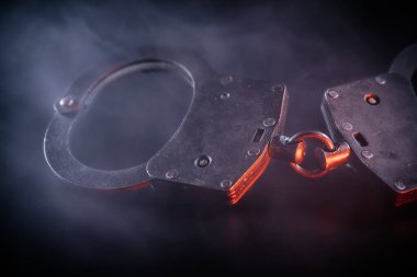 Düşük ışıkta metalik kelepçelerin yakın çekimi, kıvrımlı dumanla kaplanması, kolluk kuvvetlerinin temaları, adalet ve suçun ve cezanın karanlık yönleri.