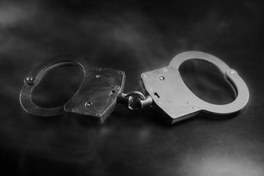 Gümüş kelepçeler, yumuşak dumanla kaplanmış karanlık bir yüzeye yerleştirilmiş, kolluk kuvvetleri ve adaleti temsil eden dramatik bir atmosfer yaratıyor.