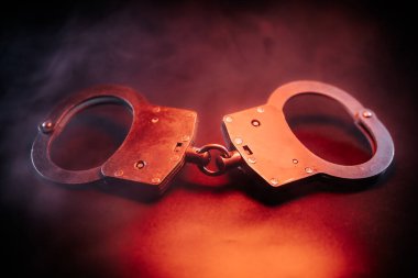 Kelepçeler, etrafta dönen dumanlarla birlikte karanlık bir yüzeye yerleştirilir. Kanun uygulama ve adalet temalarını vurgulayan dengesiz bir ortam yaratır.