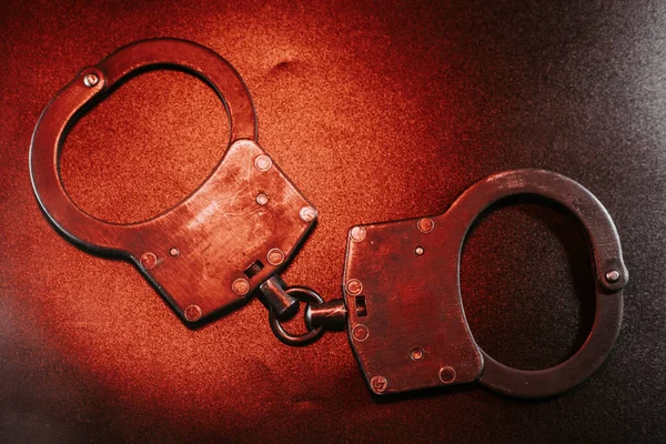 Karanlık yüzeyde metal kelepçelerin yakın çekimi, detaylı zanaat ve dokuların altını çizmek, kasvetli bir atmosferde kolluk kuvvetleri ve güvenlik temaları uyandırmak.