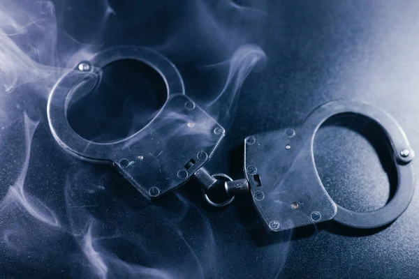 Karanlık bir yüzeye yerleştirilmiş kelepçeler, dumanla kaplanmış, kanun ve adalet temalarını vurgulayan gizemli bir ortam yaratıyor.