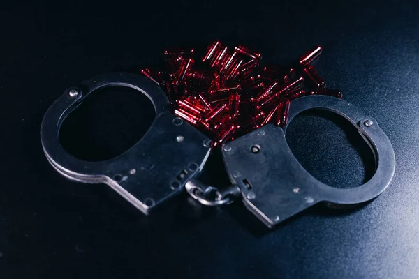 Koyu bir zemine kelepçelenmiş kırmızı boncuklar etrafa saçılmış, çarpıcı bir kontrast yaratıyor ve kanun ve düzen temaları uyandırıyor.