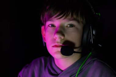 Male gamer with headset is intensely focused on screen in a dimly lit room, surrounded by vibrant lights, capturing the essence of modern gaming culture