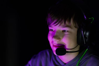 Boy wearing gaming headset, focused on screen, surrounded by vibrant lighting, demonstrating enthusiasm and engagement in a digital gaming experience