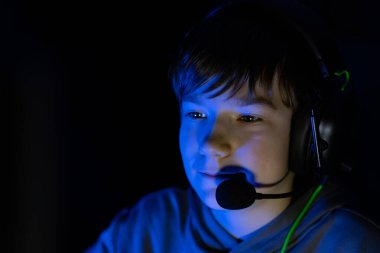 Oyun kulaklığı takan çocuk ekrana odaklanıyor, mavi ışıkla aydınlatılıyor, oyun ve dijital etkileşim için derin bir atmosfer yaratıyor.