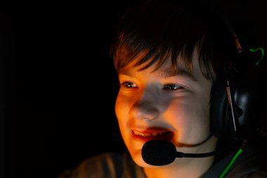 Child gamer is wearing a headset and smiling in a dimly lit environment, with soft lighting enhancing the atmosphere of enjoyment and focus in gaming
