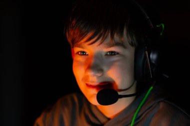 Boy wearing headset is engaged in gaming, smiling in a dimly lit room with vibrant colors, highlighting the immersive experience of modern digital entertainment