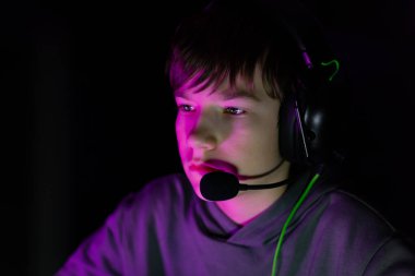 Male gamer, wearing a headset, is deeply engaged with the screen, surrounded by vibrant lighting, highlighting the excitement of gaming and digital interaction