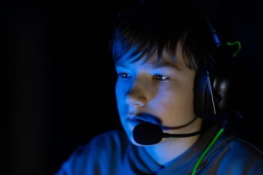 Kulaklık takan genç oyuncu, video oyununa dalmış, mavi ışıkla aydınlatılmış, odaklanma ve çağdaş bir oyun atmosferinde çarpışma gösteriyor