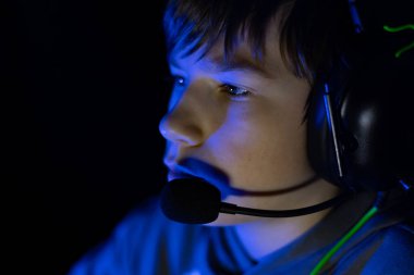 Erkek oyuncu, loş ışıklı bir ortamda yoğun bir şekilde bir video oyunuyla meşgul, mavi ışıkla vurgulanmış, modern oyun kültürünün özünü yakalıyor.