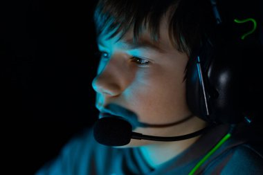 Kulaklık takan genç oyuncu, derin bir şekilde ekrana odaklanmış, yumuşak mavi ışıkla aydınlatılmış, dijital yakınlaşma ve heyecan dolu bir atmosfer yaratıyor.