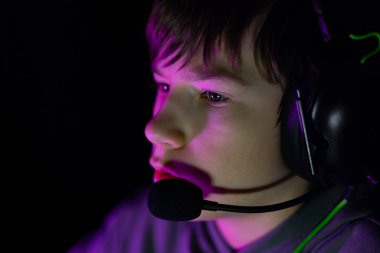 Kulaklık takan erkek oyuncu, yoğun bir şekilde canlı ışıklandırmayla ekrana odaklanmış, oyun kültürünün özünü yakalıyor ve rekabetin heyecanını yakalıyor.