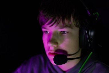 Kulaklık takan çocuk, canlı ışıklandırmayla çevrili, modern dijital atmosferi ve sanal eğlence heyecanını yansıtan bir oyun ile derinden meşgul.