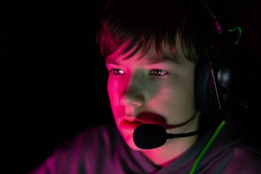 Kulaklıklı erkek oyuncu yoğun bir şekilde ekrana odaklanmış, canlı renklerle aydınlatılmış, modern oyun kültürünün özünü yakalıyor ve ilgi çekici deneyimler ediniyor.