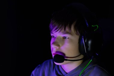 Erkek oyuncu, canlı renklerle vurgulanmış loş bir ortamda, modern oyun kültürünün özünü yakalayan bir ekranla yoğun bir şekilde meşgul.