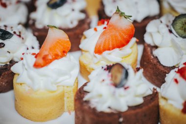 Krem şanti ve taze meyveyle süslenmiş minyatür kekler, bir tabakta zarif bir şekilde sergilenmiş, kutlama ya da özel etkinlikler için mükemmel, davetkar ve iştah açıcı.