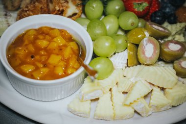 İçinde kremsi peynirler, taze yeşil üzümler ve tatlı mango turşusu bulunan gurme peynir tabağı iştah açıcı bir sunum ve enfes bir lezzet tatma deneyimi için güzelce düzenlenmiştir.