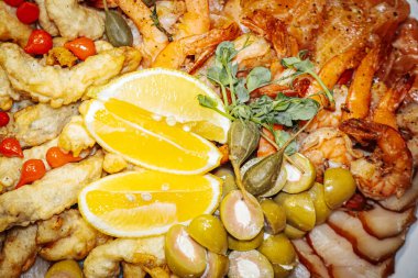 Karides, zeytin ve limon dilimli canlı deniz ürünleri tabağı, taze otlarla güzelce süslenmiş, aşçılık ilhamı için iştah açıcı bir görüntü yaratıyor.